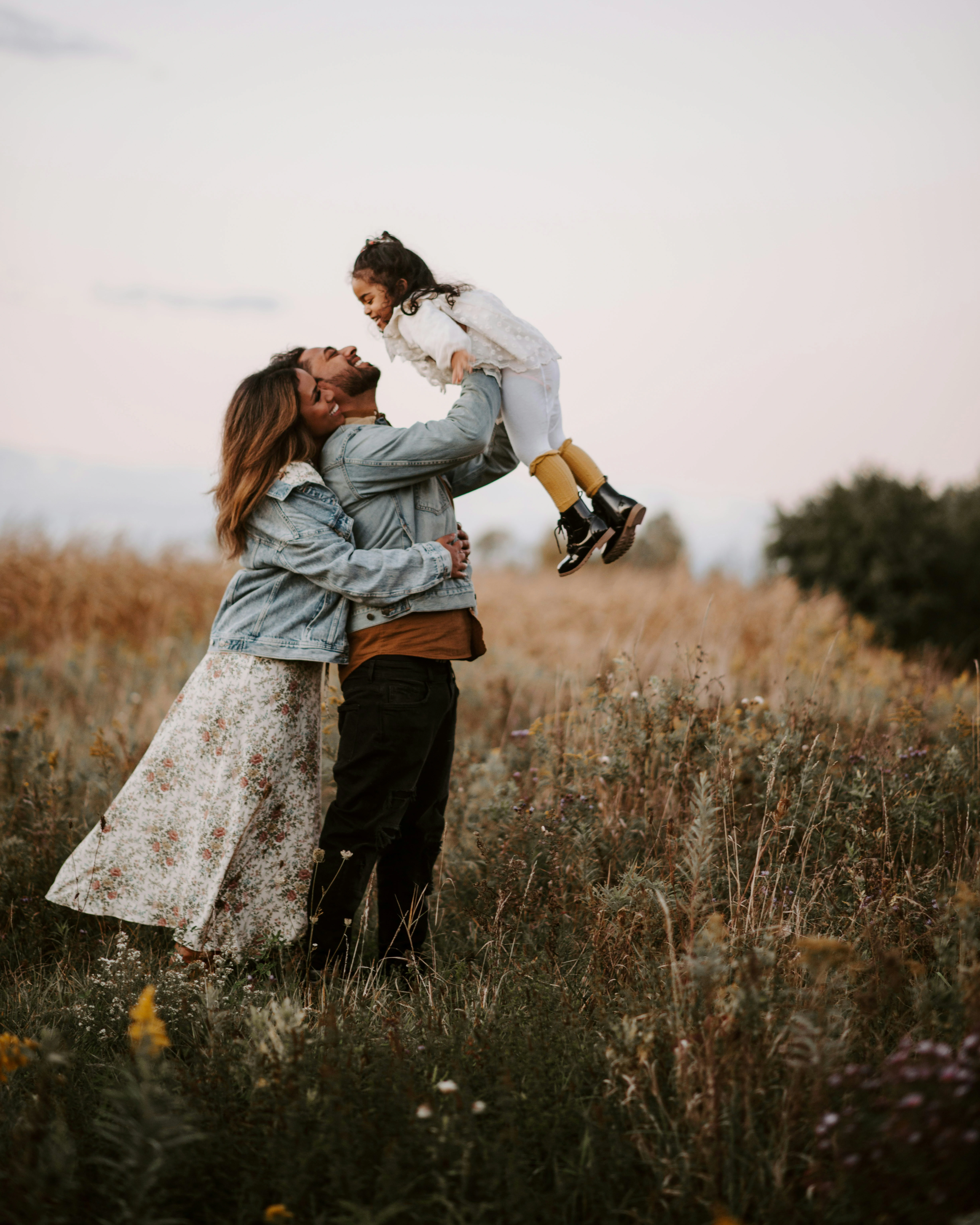 A family in a summer field, father lifting his daughter into the air